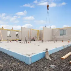 Budowa domu z prefabrykatu keramzytowego. Dźwig podnosi element ściany na fundament.