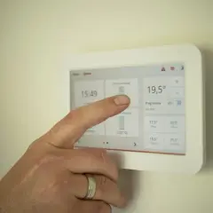 Dłoń dotyka ekranu termostatu, pokazując, jak ustawić piec gazowy kondensacyjny ekonomicznie.