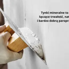 Ręce w rękawiczkach nakładają tynk na ścianę kielnią. To obrzutka, która zapewnia trwałość i paroprzepuszczalność.