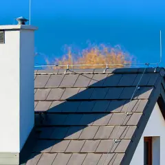 Dach z dachówką i kominem, na którym widoczna jest instalacja odgromowa. Cena takiej ochrony domu jest inwestycją w bezpieczeństwo.