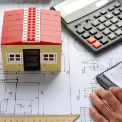 Model domu z klocków, kalkulator i notatnik z ołówkiem na planach budowlanych. Obliczanie, ile kosztuje budowa domu.