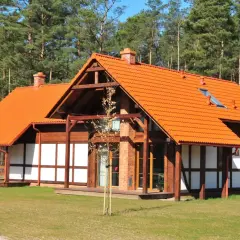 Urokliwy dom szachulcowy z pomarańczowym dachem, otoczony zielonym trawnikiem i lasem sosnowym.