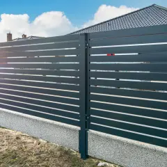 Nowoczesne ogrodzenie z ciemnoszarych paneli, co zamiast podmurówki pod ogrodzenie? Betonowy cokół z kamyczków.