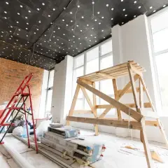 Remont pokoju: drabina, rusztowanie i materiały budowlane pod sufitem.