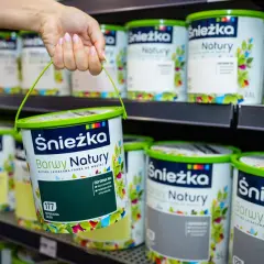 Ręka trzyma wiaderko z zieloną farbą Śnieżka Barwy Natury. Na półce widać wiele innych puszek tych farb.