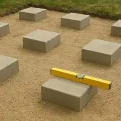 Układanie fundamentów pod taras betonowy. Kostki betonowe rozmieszczone na piasku, poziomica wskazuje idealne wyrównanie.