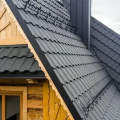 Nowoczesne dachy mansardowe z ciemnoszarej blachy falistej, otaczające drewniany dom z ozdobnymi okiennicami.