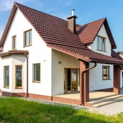 Biały dom z brązowym dachem i ceglanym cokołem. Elewacja w jasnych odcieniach to jedne z najmodniejszych kolorów elewacji, idealnie komponujące się z zielenią.