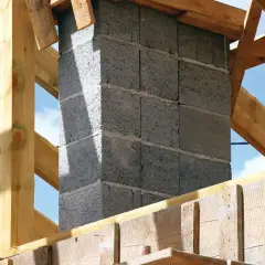 Budowa komina systemowego w trakcie. Betonowe pustaki tworzą jego ścianki, a drewniana konstrukcja dachu otacza go.