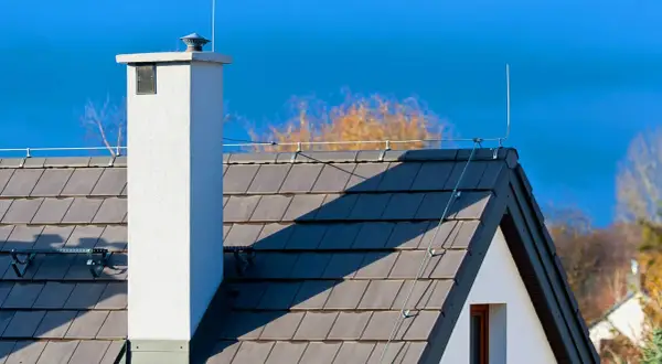 Dach z dachówką i kominem, na którym widoczna jest instalacja odgromowa. Cena takiej ochrony domu jest inwestycją w bezpieczeństwo.