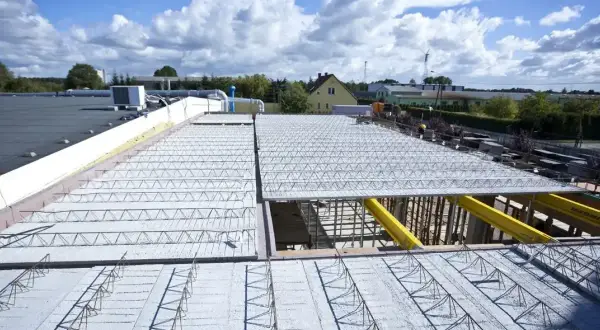 Budowa nowego stropu nad halą przemysłową. Metalowe kratownice i zbrojenie czekają na beton.