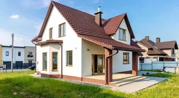 Biały dom z brązowym dachem i ceglanym cokołem. Elewacja w jasnych odcieniach to jedne z najmodniejszych kolorów elewacji, idealnie komponujące się z zielenią.