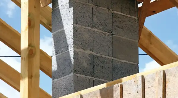 Budowa komina systemowego w trakcie. Betonowe pustaki tworzą jego ścianki, a drewniana konstrukcja dachu otacza go.