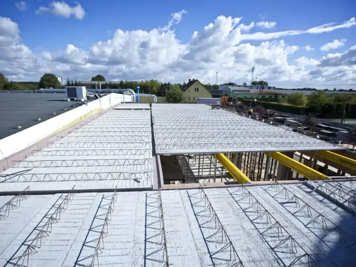 Budowa nowego stropu nad halą przemysłową. Metalowe kratownice i zbrojenie czekają na beton.