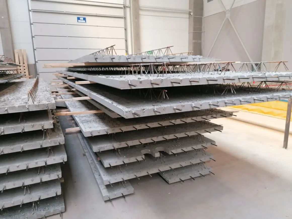 Stos prefabrykowanych płyt betonowych z widocznym zbrojeniem, przypominającym delikatny filigran.