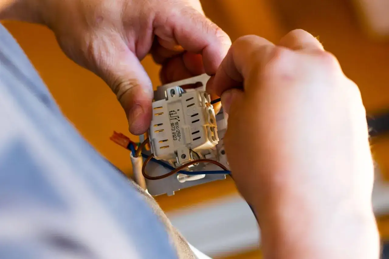 Ręce montują mechanizm włącznika. Zastanawiasz się, ile za punkt elektryczny? To praca dla fachowca.