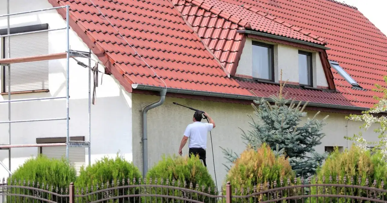 Mężczyzna na rusztowaniu myje elewację domu myjką ciśnieniową. To prawdziwa obrzutka z wodą, by przywrócić blask ścianom.
