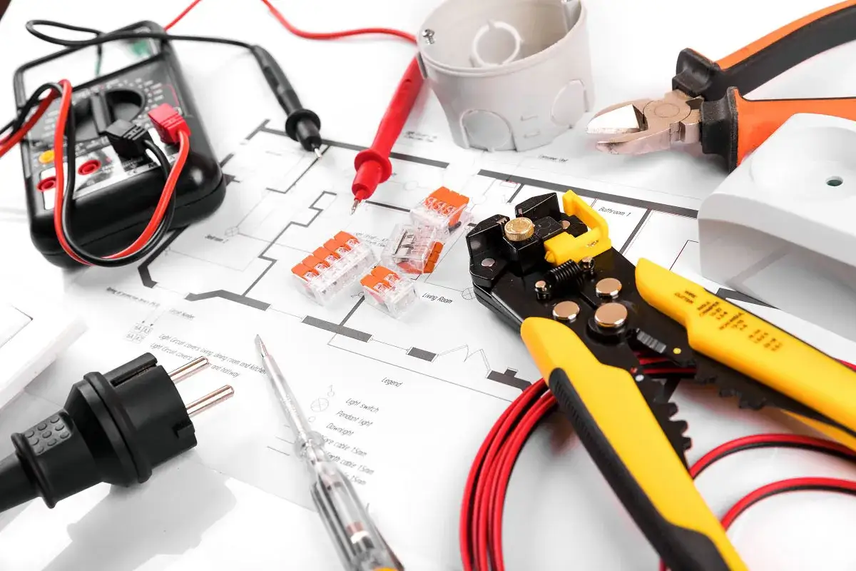 Narzędzia elektryczne i schemat instalacji. Multimetr, ściągacz izolacji, złączki, wkrętak, wtyczka i obcinaczki – wszystko do obliczenia koszt instalacji elektrycznej.