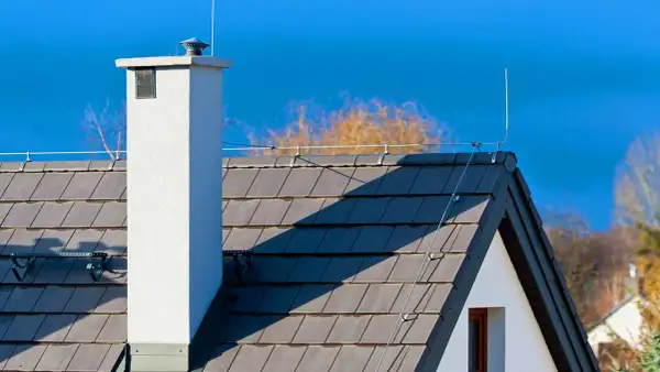 Dach z dachówką i kominem, na którym widoczna jest instalacja odgromowa. Cena takiej ochrony domu jest inwestycją w bezpieczeństwo.