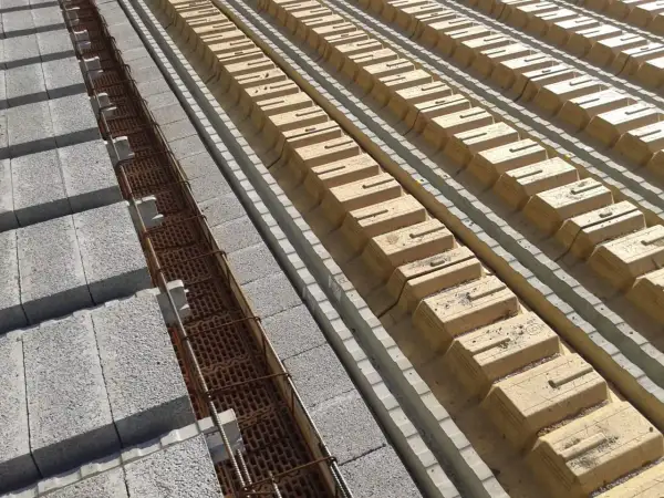 Budowa stropu DZ 3: betonowe pustaki i zbrojenie w rowkach, obok żółte pustaki szalunkowe.