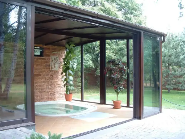 Relaks w domu: przestronny **ogród zimowy** z jacuzzi, kamienną ścianą i zielenią.